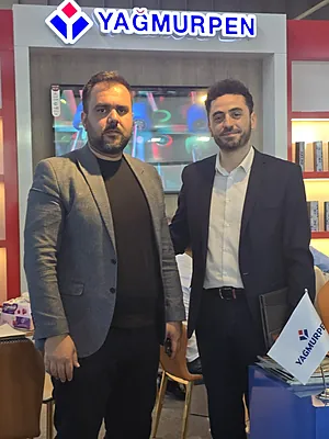 Two men in suits standing in front of a YAĞMURPEN sign inside a modern office or showroom.