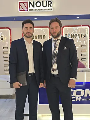 Two men in business suits standing in front of a booth with a Nour Electrical Industries sign.
