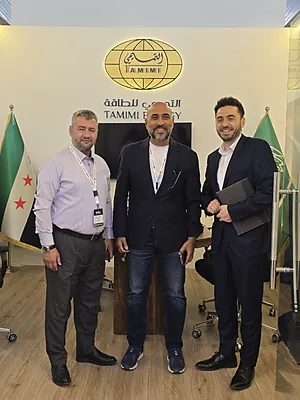 Three men in business attire standing in front of a sign reading Tamimi Energy with flags on each side.