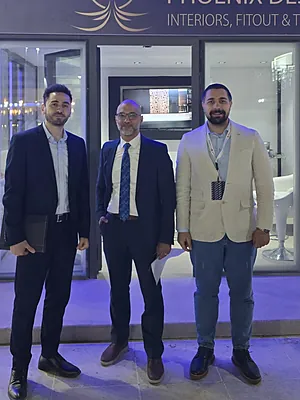 Three men in business attire standing outside a modern showroom with glass doors at night.