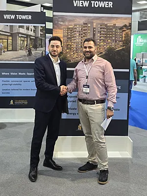 Two men shaking hands at a real estate exhibition booth with a 'View Tower' banner behind them.