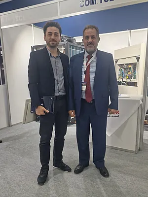 Two men in business attire standing side by side at an indoor exhibition booth.