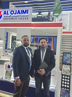 Two men in business attire standing inside a booth of Al Ojaimi Empower House at an event.