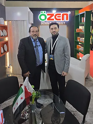 Two men posing in business attire in front of an Özen Born Turkey booth at an event.