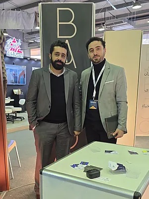 Two men in suits standing at a trade show booth with a table and promotional materials.