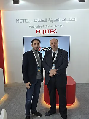 Two men in business attire standing in front of a Fujitec authorized distributor display.