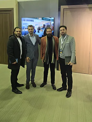 Four men standing indoors in business casual to formal attire, smiling toward the camera.
