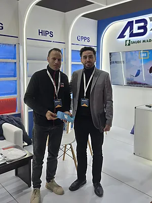 Two men standing in a trade show booth with tech displays and lanyards around their necks.